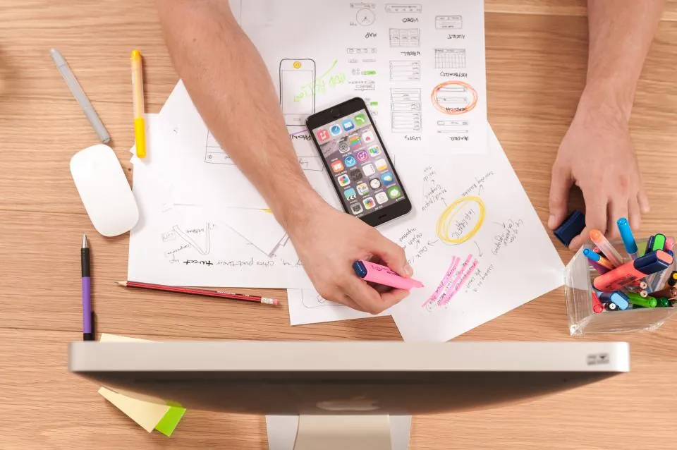 Hands sketching website wireframes on paper beside a phone